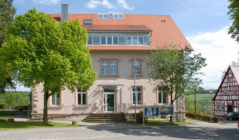 Auf der Seite zum Thema Lkw-Fahrer in Hohenlohe sieht man das Rathaus von Krautheim. Links ein Baum im Frühlingsgrün, rechts ein Fachwerkhaus. Das Wetter ist perfekt, die Sonne scheint.