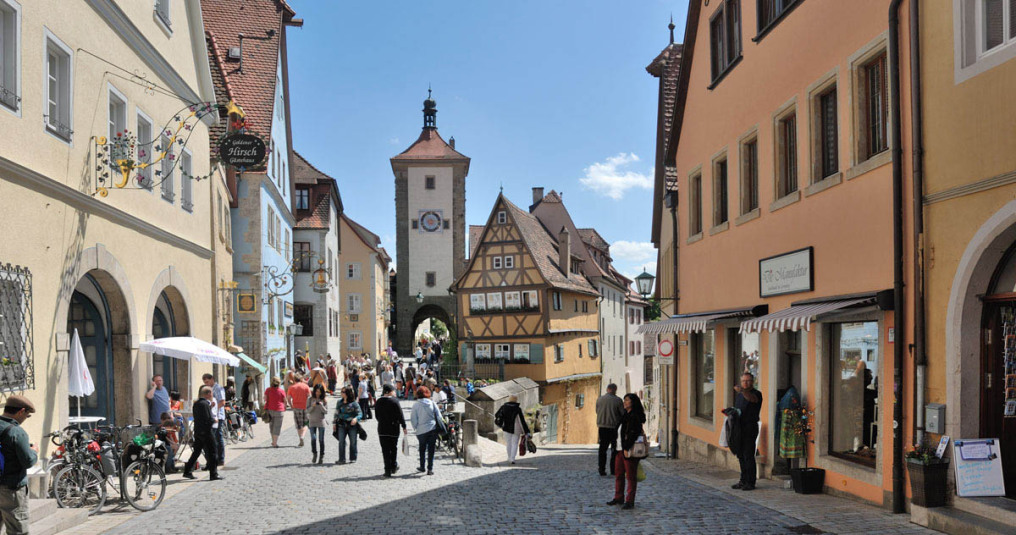 Die bekannteste Aufnahme in Rothenburg ob der Tauber: Es ist der berühmt te Stadtturm mit dem kleinen, spitzen Fachwerkhaus davor. Rechts und links bilden zwei historische Gebäude die Straßenschlucht, in der viele Touristen bummeln.