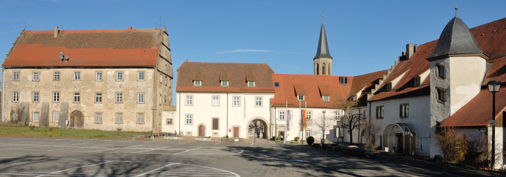 Die Schlossanlage in Ravenstein von der Innenseite betrachtet. Die rechten beiden Drittel des Ensembles sind renoviert, das linke Drittel ist noch in hellbraunem verwitterten Stil. Hinter dem Ensemble sieht man einen Kirchturm. Zwei Bäume sind unbelaubt,